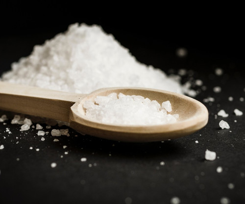 The image shows Kosher salt on a black background and on a spoon
