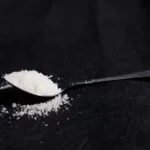 A pile of salt on a spoon on a black table.