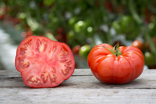 This picture shows two tomatoes. One is cut in half, and the other one is whole.